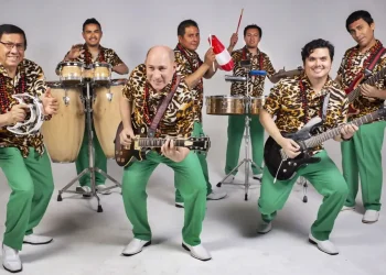 Grupo musical posando con instrumentos, vestidos con camisas estampadas y pantalones verdes en un estudio
