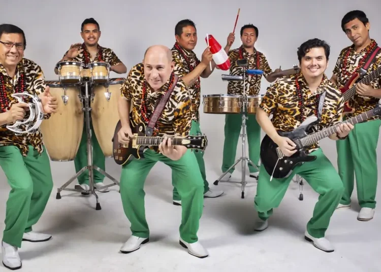 Grupo musical posando con instrumentos, vestidos con camisas estampadas y pantalones verdes en un estudio