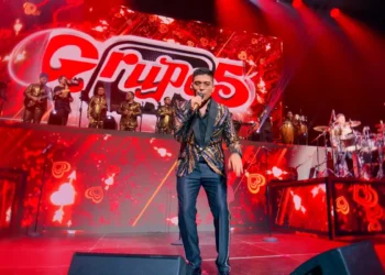Christian Yaipén cantando en un concierto del Grupo 5 en un escenario con luces rojas