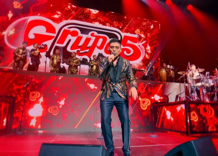 Christian Yaipén cantando en un concierto del Grupo 5 en un escenario con luces rojas