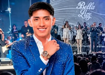 Oscar Junior sonriente con saco azul brillante y reloj, frente al escenario de la orquesta Bella Luz