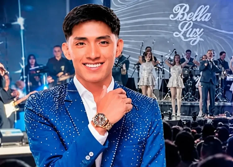 Oscar Junior sonriente con saco azul brillante y reloj, frente al escenario de la orquesta Bella Luz